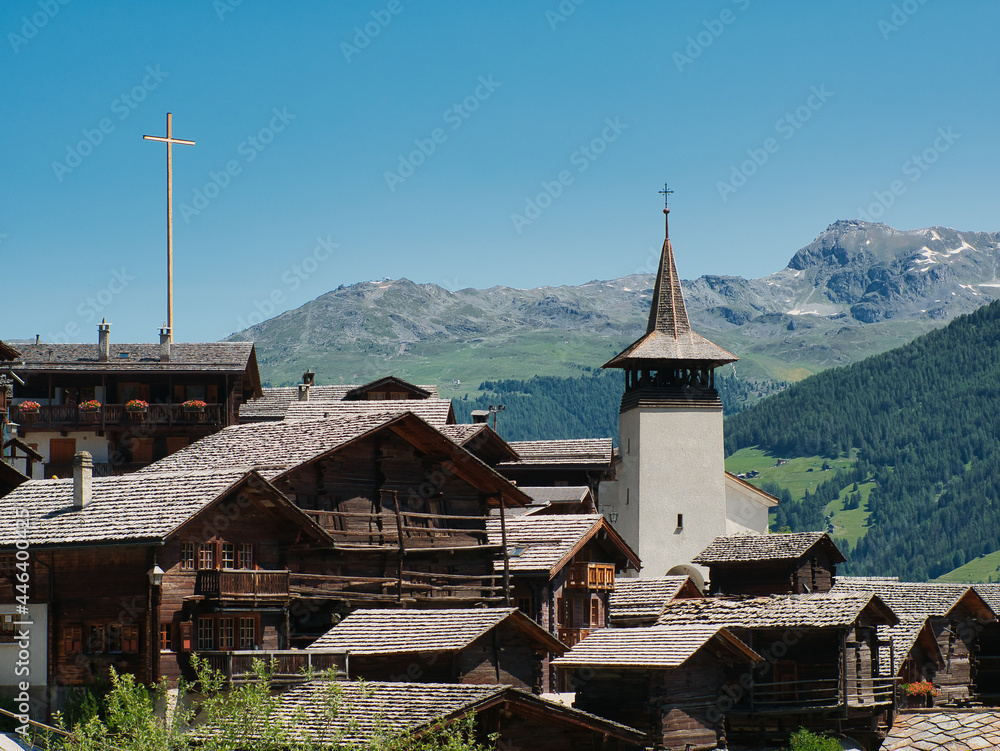 View of traditional wooden houses, also called Swiss chalet, and the church tower in the village of Grimentz, in the canton of Valais (Switzerland), municipality of Anniviers. Alps in the background.