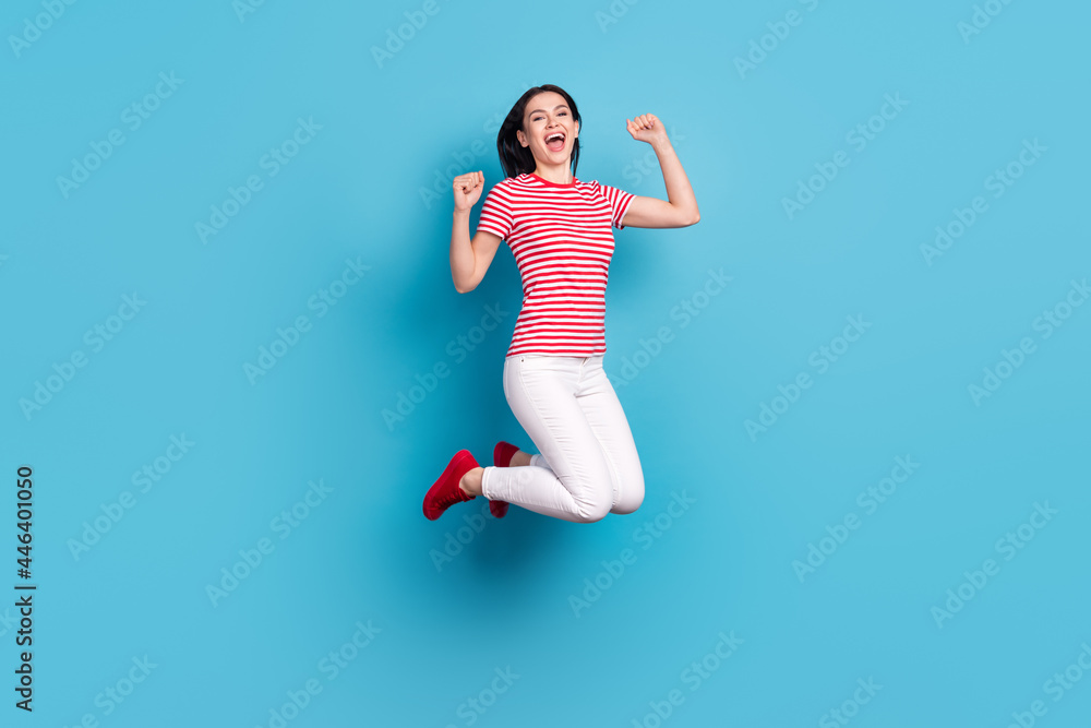 Full body profile side photo of young girl happy positive smile jump rejoice victory fists hands isolated over blue color background Full body profile side photo of young girl happy positive smile jump rejoice victory fists hands isolated over blue color background