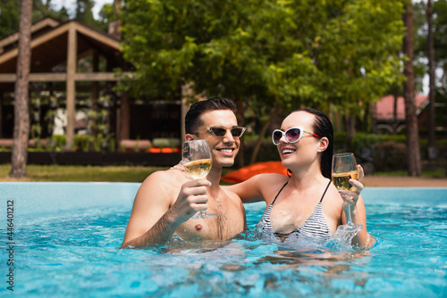 Young couple with wet hair holding wine in swimming pool
