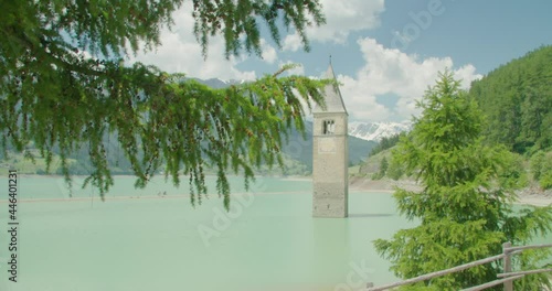 Medium shot, Tree branch blowing in the wind in Italy, Kirchturm von Altgraun on the lake of Reschensee in the background. photo