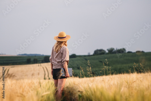 Farmer inspecting and examining agricultural field before harvest. Woman with straw hat and digital tablet standing in barley field