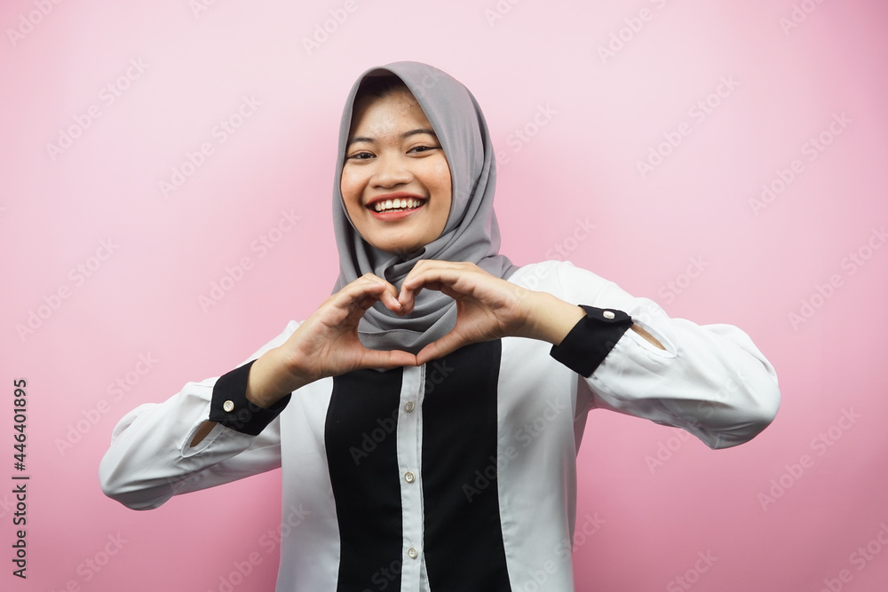 Beautiful asian young muslim woman smiling confident, enthusiastic and cheerful with hands sign of love, affection, happy, on chest isolated on pink background Beautiful asian young muslim woman smiling confident, enthusiastic and cheerful with hands sign of love, affection, happy, on chest isolated on pink background