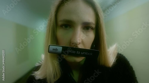Caucasian blonde woman in a fur coat stands in an underground passage, looks into the camera and holds a sign in her mouth with the inscription - Slide to unlock