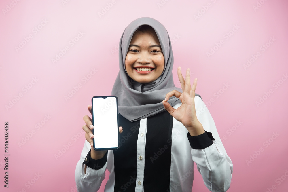 Beautiful young asian muslim woman smiling confidently and excitedly with hands holding smartphone, presenting application, ok sign hand, good job, success, isolated on pink background Beautiful young asian muslim woman smiling confidently and excitedly with hands holding smartphone, presenting application, ok sign hand, good job, success, isolated on pink background