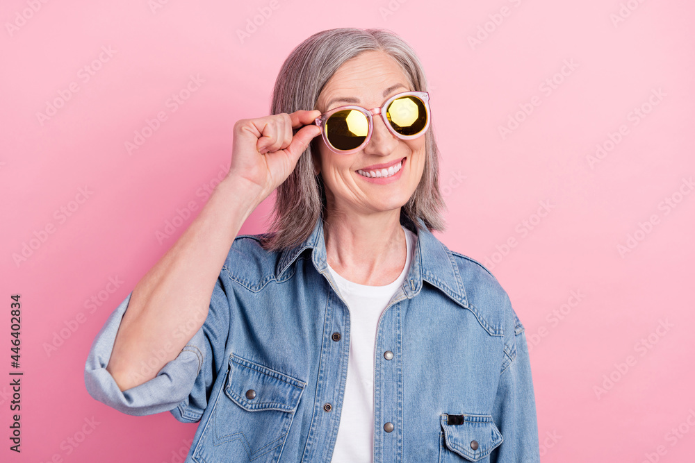 Photo of funny elder lady hand eyewear look empty space wear blue shirt isolated on pink color background Photo of funny elder lady hand eyewear look empty space wear blue shirt isolated on pink color background