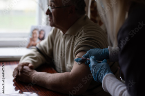Young woman doctor injecting vaccine to elderly man during home visit