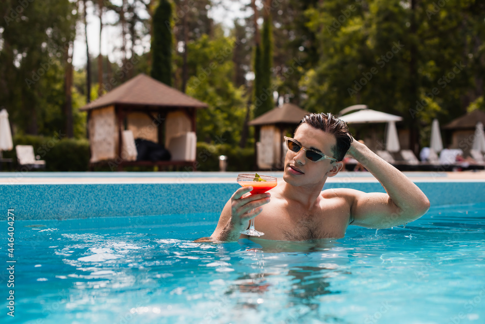 Man with cocktail resting in swimming pool on resort