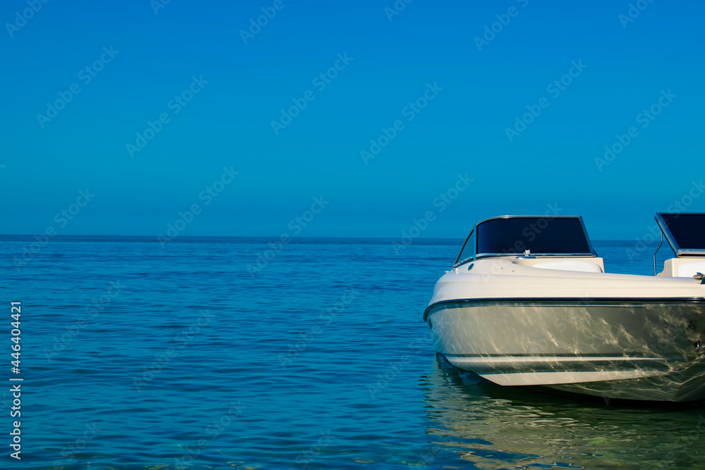 a white boat standing on the sea water against the blue sky. The background is blurred. Part of the boat