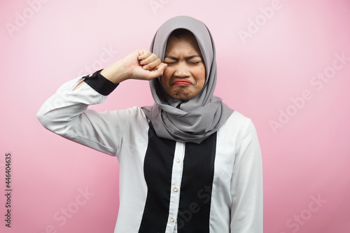 Beautiful young muslim woman crying, hands wiping tears, isolated on pink background