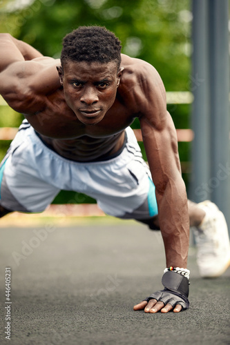 Athlete doing push-ups on the sports ground, African American athlete doing push-ups on outdoor gym equipment, sports lifestyle, striving for success