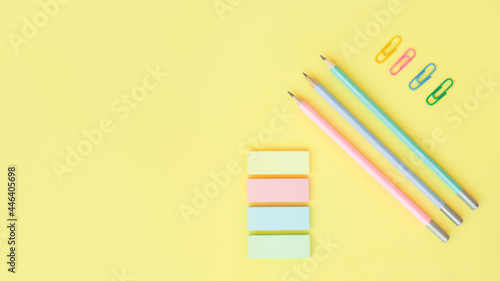 office supplies on a yellow background with copy space. Graphite pencils, paper clips and sticky notes