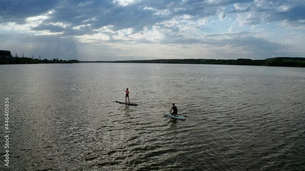 Two stand up paddlers enjoying vacation. Aerial view of active couple stand up paddling together Two stand up paddlers enjoying vacation. Aerial view of active couple stand up paddling together