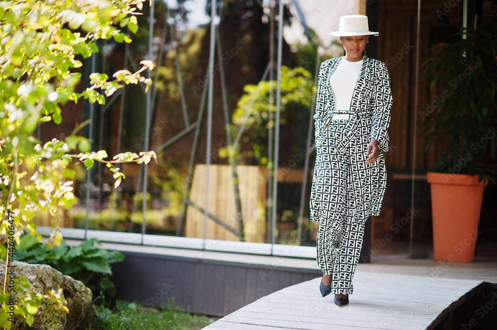 Fototapeta premium Beautiful african american woman natural makeup wear fashion clothes casual black and white dress code office style total blouse and pants suit and hat.