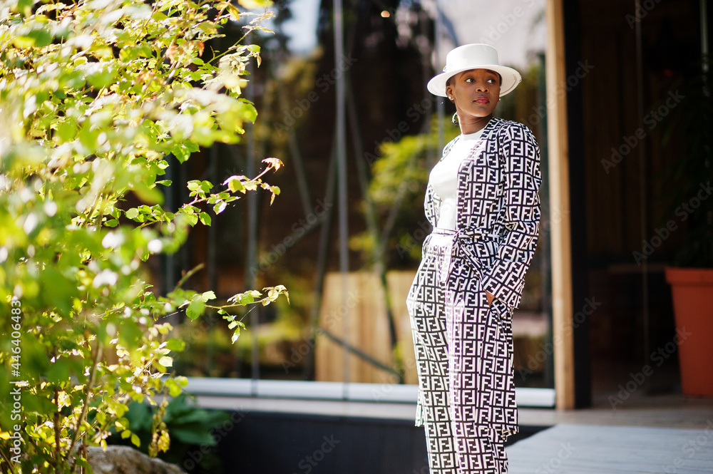 Fototapeta premium Beautiful african american woman natural makeup wear fashion clothes casual black and white dress code office style total blouse and pants suit and hat.