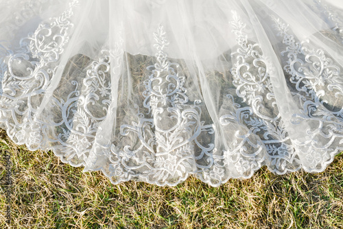 Détail de la traîne en dentelle d'une robe de mariée étalée sur l'herbe en extérieur