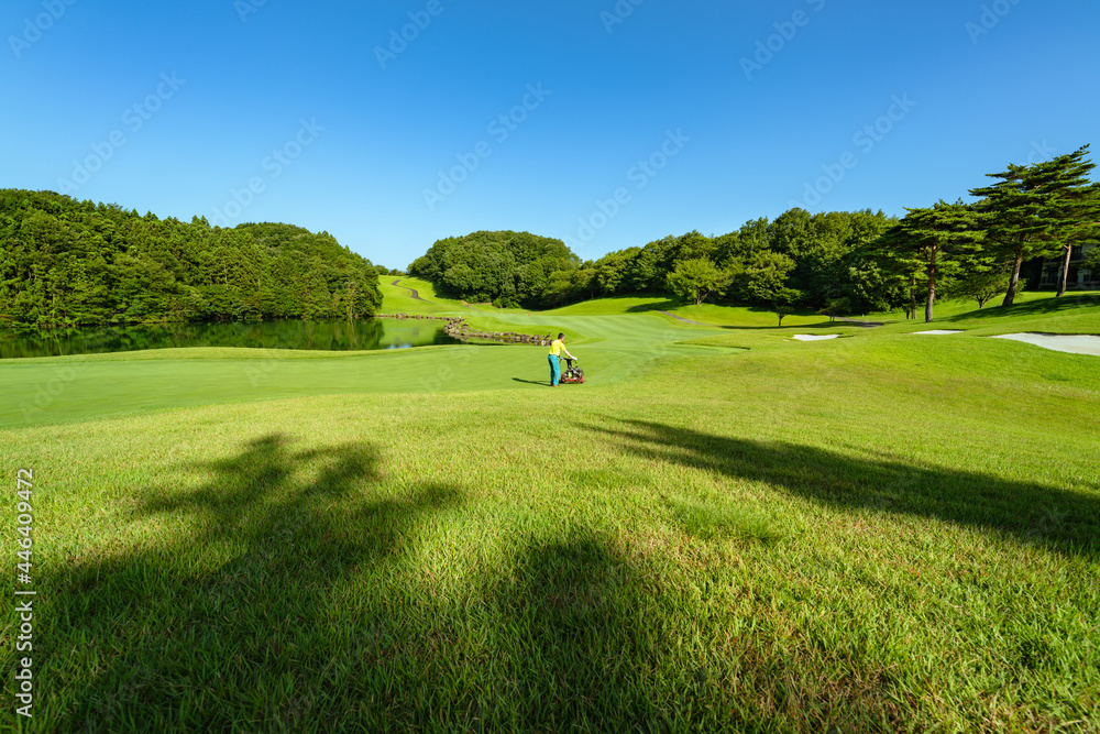 Obraz premium 早朝のゴルフ場と芝を刈るグリーンキーパー