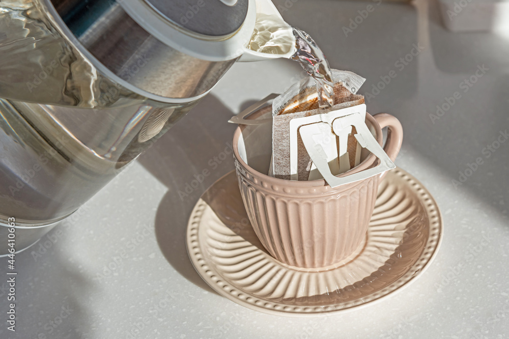 Drip brewing coffee. Pouring hot water into cup with drip coffee bag on white marble table, closeup Drip brewing coffee. Pouring hot water into cup with drip coffee bag on white marble table, closeup