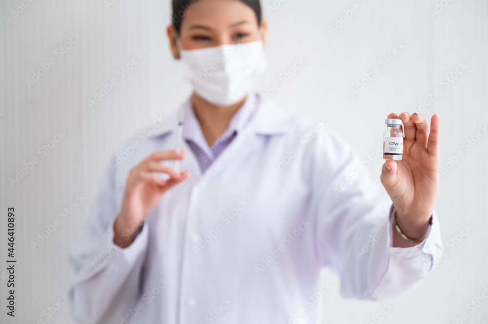 Female doctor wearing a mask stands holding a syringe with a vaccine. Coronavirus19 in the laboratory. Concept of protection against the COVID-19 virus. Female doctor wearing a mask stands holding a syringe with a vaccine. Coronavirus19 in the laboratory. Concept of protection against the COVID-19 virus.