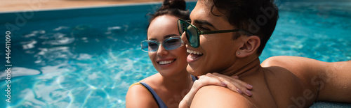 Smiling woman embracing boyfriend in swimming pool on blurred background, banner