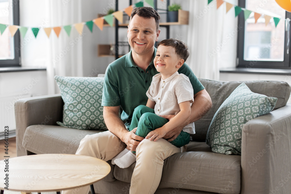 family, fatherhood and people concept - portrait of happy smiling father and little son sitting on sofa at home party