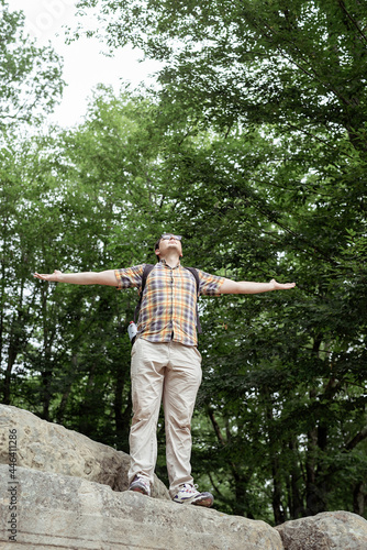 Young man standing on a big rock in the forest looking away