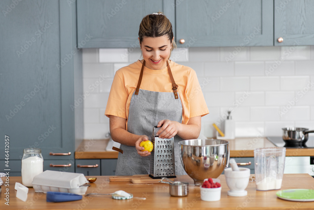 culinary, baking and people concept - happy smiling young woman cooking food on kitchen at home and grating lemon peel on grater culinary, baking and people concept - happy smiling young woman cooking food on kitchen at home and grating lemon peel on grater