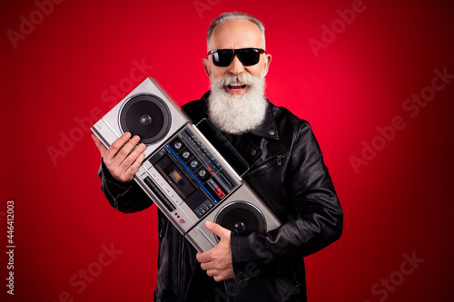 Portrait of attractive cheerful grey-haired man deejay hugging tape player free time isolated over bright red color background