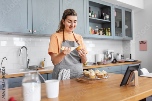 culinary  bake and cooking food concept - happy smiling young woman with baking bag making cupcake topping on kitchen at home