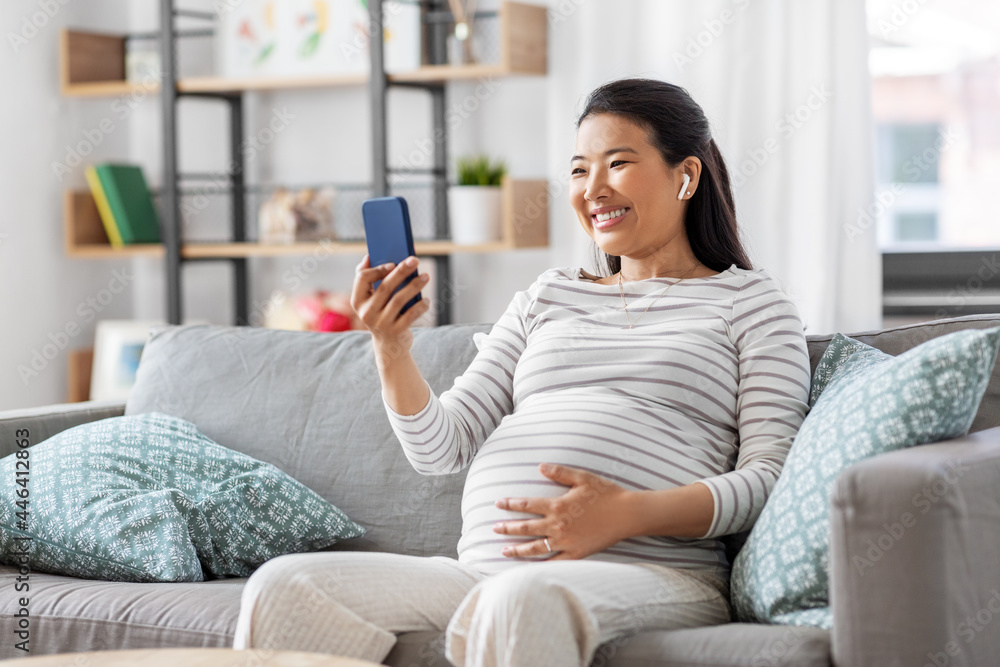 pregnancy, rest, people and expectation concept - happy smiling pregnant asian woman with smartphone and earphones sitting on sofa at home and listening to music pregnancy, rest, people and expectation concept - happy smiling pregnant asian woman with smartphone and earphones sitting on sofa at home and listening to music