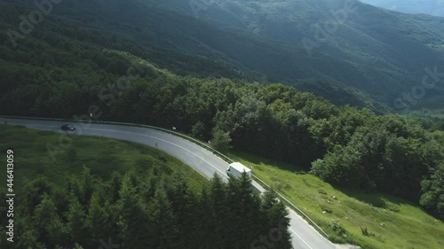 Drone following white cargo van driving along mountain road with dense evergreen frorest photo