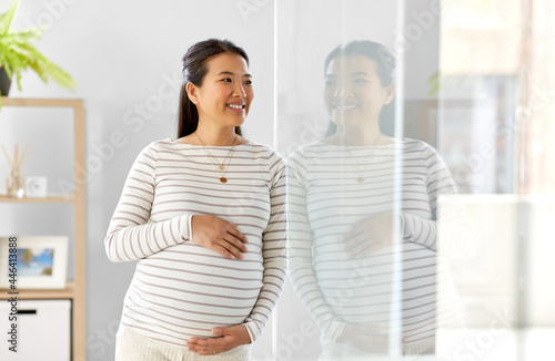 pregnancy, rest, people and expectation concept - happy smiling pregnant asian woman touching her belly at home