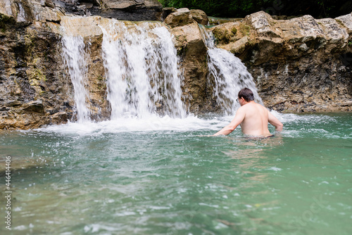 Fototapeta Naklejka Na Ścianę i Meble -  Man swimming in the mountain river with a waterfall