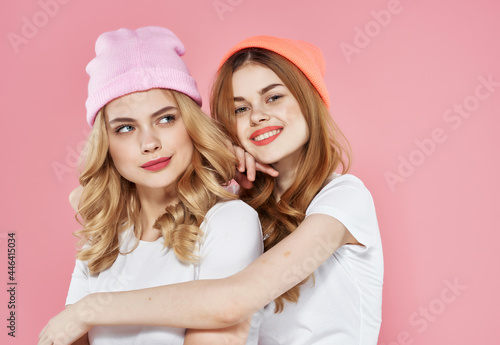 cheerful girlfriends in white t-shirts after clothes hug friendship pink background