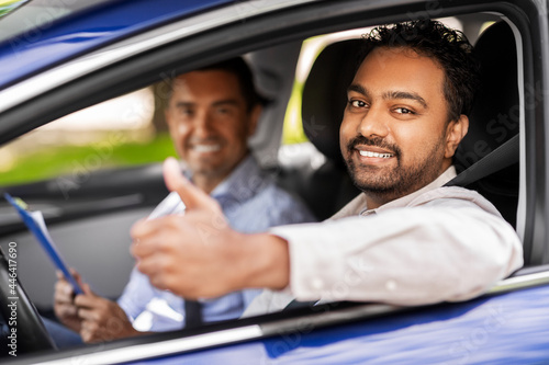 driver courses, exam and people concept - happy smiling indian man showing thumbs up and driving school instructor with clipboard in car © Syda Productions
