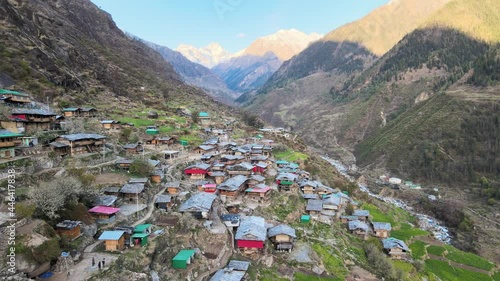 Osla. beautiful smooth slow aerial drone shot view of village on himalaya mountains at sunset sunrise. blue water river flowing through valley. colorful huts houses. snow covered mountain background