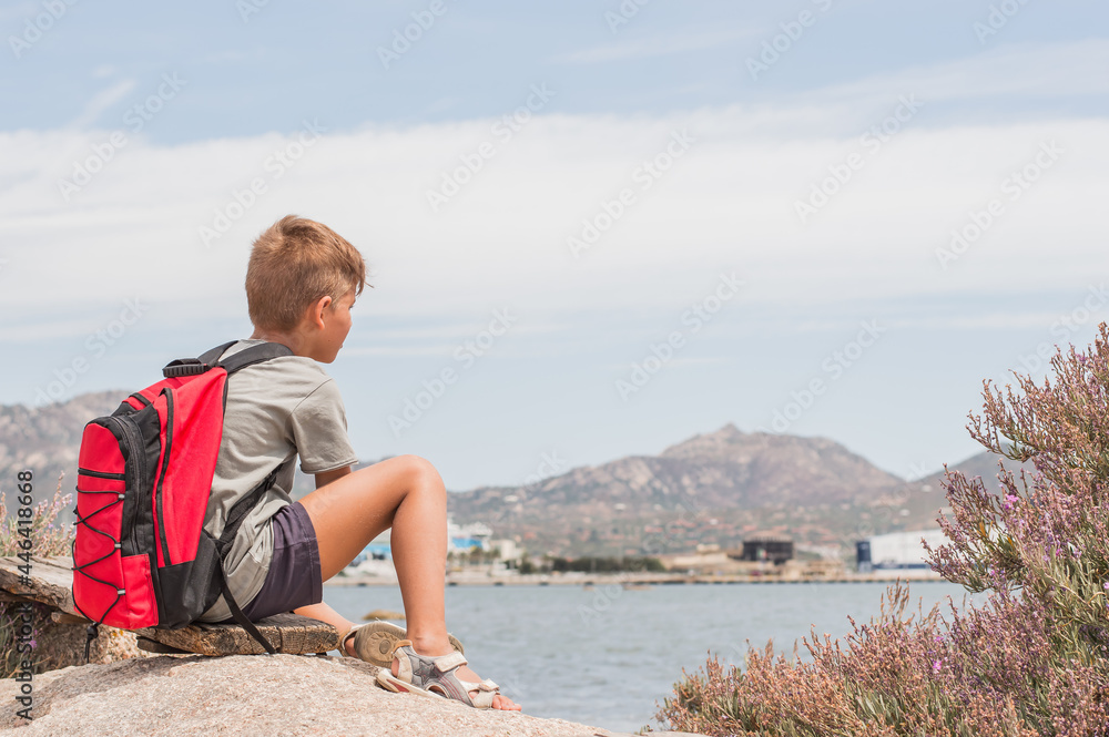 a boy with a backpack looks into the distance at a port at sea