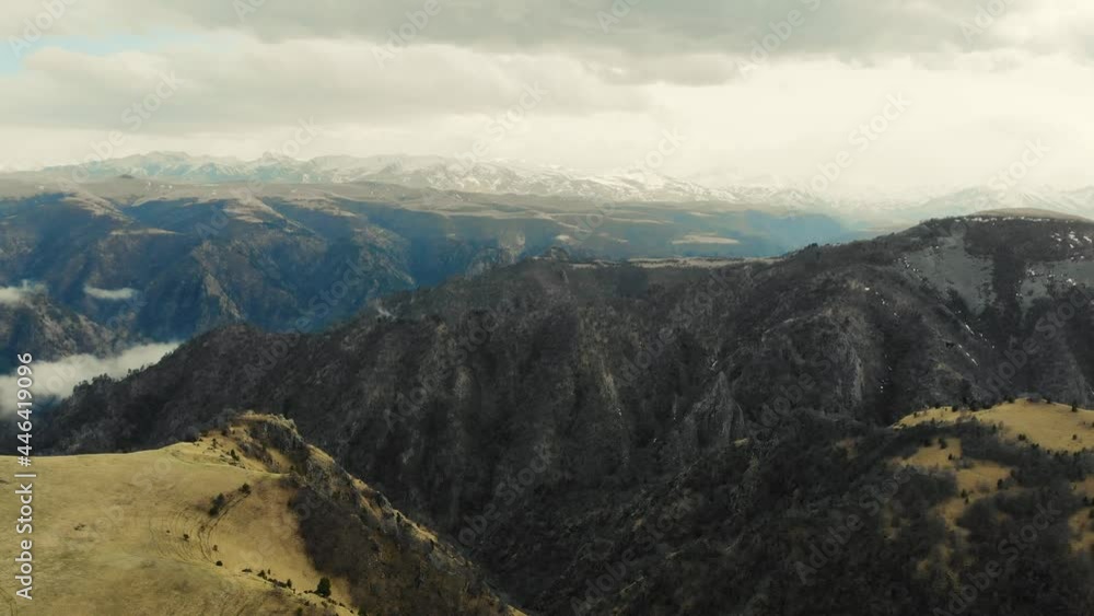 Aerial view of Caucasus Mountains. Gray sky is visible over green meadows. White clouds form river. Peaks of sharp mountains are covered with glaciers and snow in the distance. Cloudy weather Aerial view of Caucasus Mountains. Gray sky is visible over green meadows. White clouds form river. Peaks of sharp mountains are covered with glaciers and snow in the distance. Cloudy weather