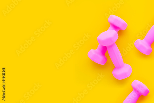 Top view of pink dumbbells on yellow background. Copy space