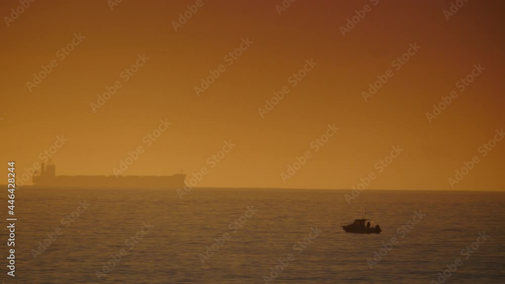Seascape at early morning with fishing boat and cargo container industrial ship on horizon. Mediterranean sea in Spain. Seascape at early morning with fishing boat and cargo container industrial ship on horizon. Mediterranean sea in Spain.