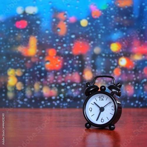 Selective focus image of alarm clock on wooden table against rainy day window background