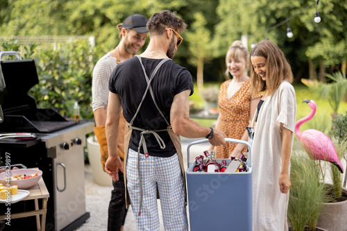 Friends with fridge full of alcohol at party outdoors, young people gathering for a picnic, carrying alcohol drinks at backyard