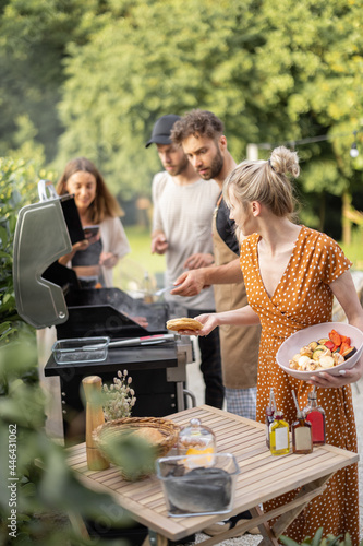 Fotografie Happy young friends hanging out together, grilling vegetables and meat on a modern grill at picnic