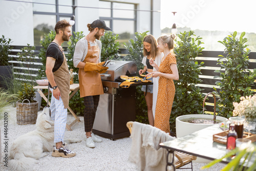 Foto Happy young friends hanging out together, grilling food on a modern grill at beautiful backyard of a country house
