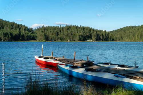 Quay with kayaks on a lake and mountain landscape with forest and blue sky with clouds, Shiroka Polyana dam, Bulgaria
