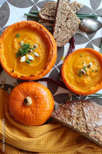 Creamy, nourishing butternut squash soup with a hunk of crusty bread. Fall comfort food. Healthy eating concept. Top view photo of beautiful orange soup served in a squash bowl. 