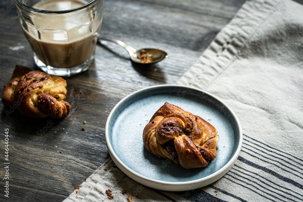 Φωτογραφία Cinnamon yeast knot bun on blue plate and glass of coffee with milk on dark wooden table