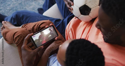 Composite of father and son at home watching sports event on smartphone photo