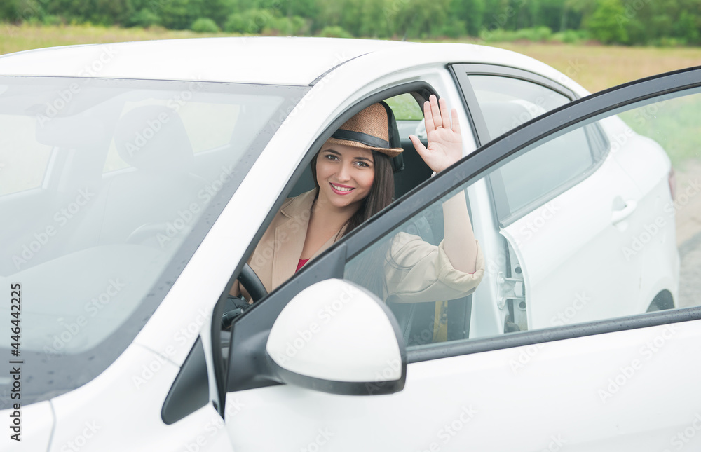 Beautiful happy young woman with hat sitting in the white car on the road