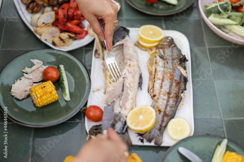 People eating healthy food outdoors  grilled fish and vegetables on a green table  close-up