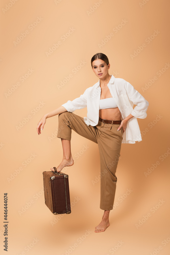 barefoot woman in stylish clothes stepping on retro suitcase on beige background barefoot woman in stylish clothes stepping on retro suitcase on beige background